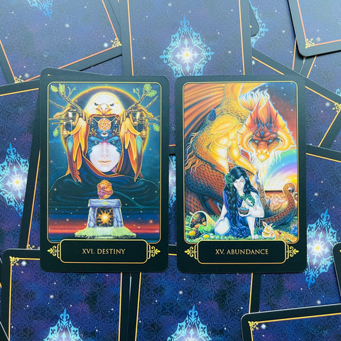 tarot kortos su tamsiai mėlynu fone ir aukso rėmeliais, artimas planas, dvi atverstos kortos Destiny (XVI) ir Abundance (XV)
