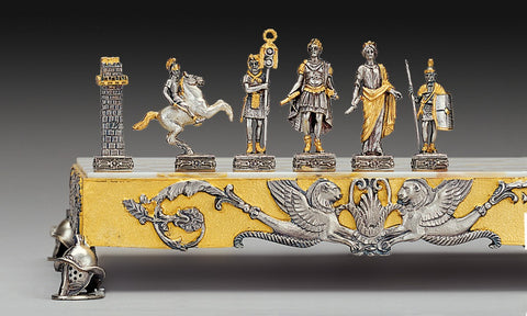 Šachmatai su sidabrinėmis ir auksuotomis antikinėmis figūrėlėmis, arti kadro parodytas puošnus lentos kraštas