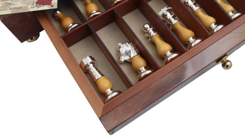 Šachmatų figūrėlės su medinėmis rankenomis ir sidabrinėmis detalėmis, išdėstytos skyriuotame mediniame dėkle, matomas žirgo profilis iš arti