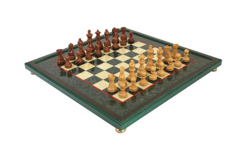 Šachmatai ant žaliai raštuotos lentos su šviesiomis ir tamsiomis medinėmis figūromis ir pakeltais auksiniais kojelėmis, iš kampo