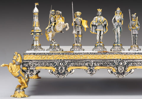 Šachmatų rinkinys aukso ir sidabro tonų, artimas kampinis kadras ant dekoratyvaus, raižyto stovo