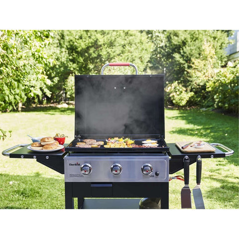 Dujinė kepsninė Char‑Broil, nerūdijančio plieno ir juoda apdaila, trijų degiklių, atidarytu dangčiu kepanti burgers ir daržoves sode