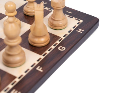 Šachmatų lenta medinė, tamsaus rudo ir šviesaus medžio kampas su F–H raidėmis ir šviesiomis figūromis, artimas planas