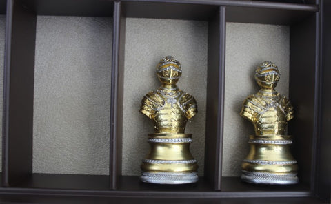 šachmatų figūra: dvi auksinės šarvuotos statulėlės stovi atskirose tamsios medienos nišose; centrinė ir dešininė skiriasi kampu