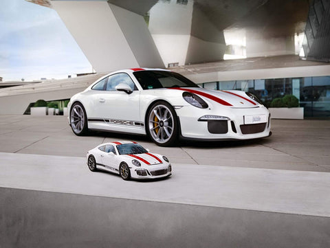 Porsche 911 modelis miniatiūrinis baltas su raudonomis juostomis, dėlionės variantas, rodantis mastelį prieš tikrą automobilį