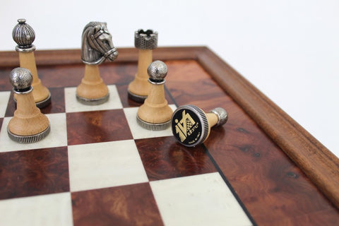 Šachmatų rinkinys medinis su metalinėmis figūrėlėmis, artimas kampinis kadravimas rodantis nugriuvusį juodą karalių ir apdailos rėmą