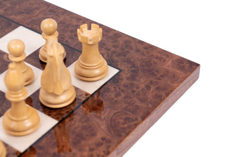 Šachmatai su šviesiomis medinėmis figūromis ant blizgios riešuto rašto šachmatų lentos kampo, detalė