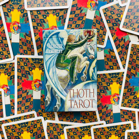 Centrinė Aleister Crowley Thoth Tarot dėžutė ant spalvoto kortų fono, priekinis viršelis ir detalus dizainas aiškiai matomi