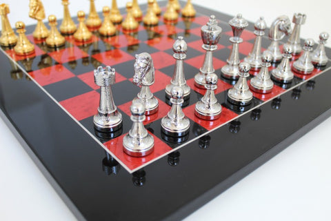 Šachmatai su sidabrinėmis ir auksinėmis metalinėmis figūromis ant juodo-raudonos blizgios lentos, artimas dešinės pusės kadravimas
