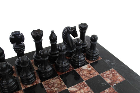 Šachmatai iš juodo marmuro su rudo‑juodo marmuro lenta, artimas kampinis kadras rodantis galines figūras