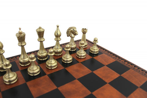 Šachmatai su aukso spalvos metalinėmis figūromis ant rudos‑juodos medinės lentos; artimas kampinis kadravimas akcentuoja detales
