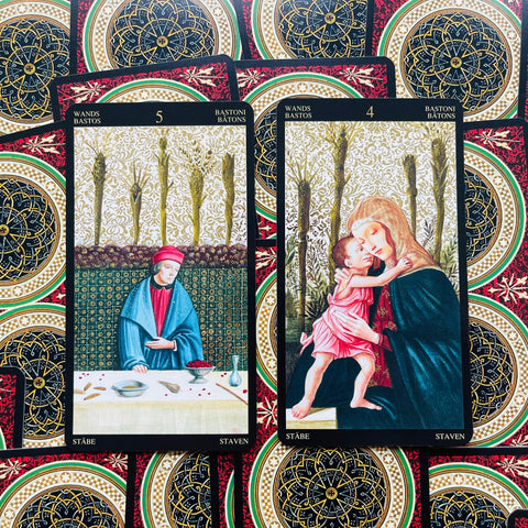 tarot kortos su aukso ornamentais, dvi iš arti parodytos kortos — Penki lazdelės (sėdintis vyras) ir Keturi lazdelės (motina su kūdikiu), akcentuoti detalūs raštai