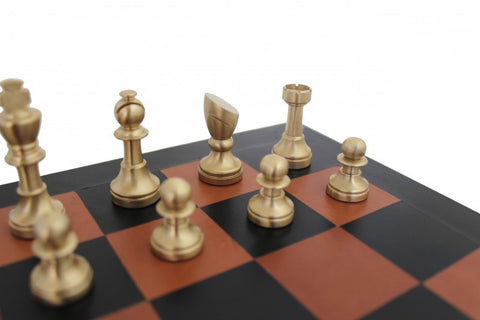 Šachmatų rinkinys su auksinio metalo figūromis ir rudos–juodos medžio imitacijos lenta, artimas kampinis planas