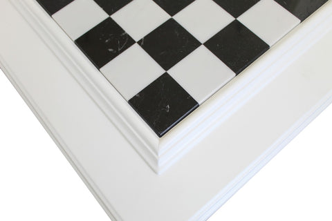 Plytelės juodai baltos šachmatinės mozaikos kampas su balta medžio profilio apdaila, rodoma iš arti ir pabrėžiant siūles