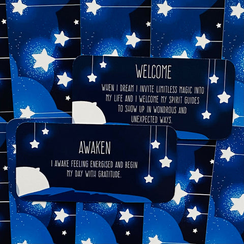 Afirmacijų kortelės mėlynoje nakties temoje su kabinančiomis žvaigždėmis, matomi „Awaken“ ir „Welcome“ variantai