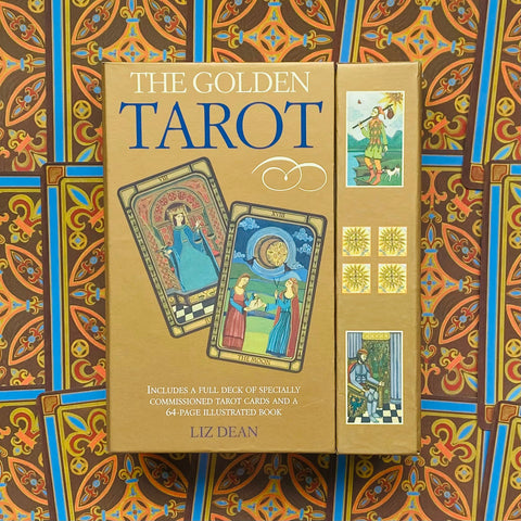 Produkto puslapis – Liz Dean „The Golden Tarot“ auksinės rudos dėžutės priekinis ir šoninis vaizdas su dviem kortomis ant ornamentuoto fono