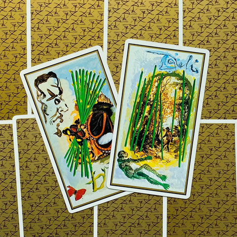 Tarot kortos su atverstu priekiu, dvi kortos demonstruoja žalias lazdeles ir aukso‑žalsvą siurrealistinį piešinį