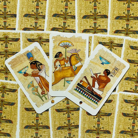 Tarot kortos egiptietišku dizainu ant senovinio papiruso fono, trys išskirtinės kortos išdėstytos virš komplekto, tinkamos būrimui