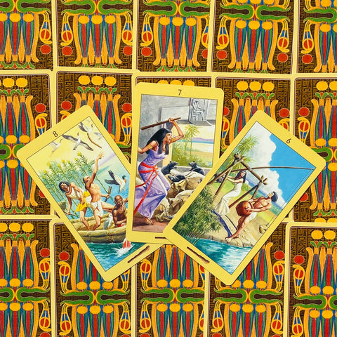 tarot kortos Egipto tematika, trys atverstos geltonu kraštu kortos centre ant spalvingų nugarėlių, rodo 6–8 Lazdų kortas
