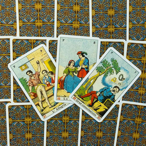 Tarot kortos plokščiai išdėstytos, matyti aukso‑mėlyna nugarėlės raštas ir trys atverstos kortos centre fane