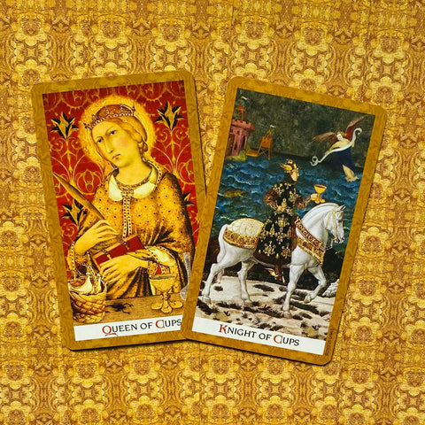 Tarot kortos — dvi atverstos auksuotos kortos (Karalienė taurėms ir Riteris taurėms) ant ornamentuoto aukso fono, matomos iš viršaus