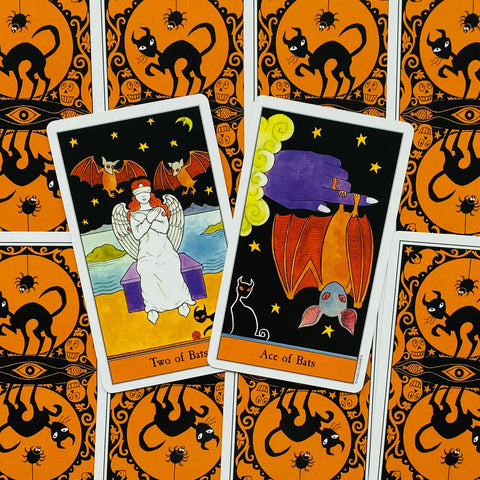 Tarot kortos su oranžinėmis‑juodomis katės nugarėlėmis, dvi atverstos kortos (Two of Bats ir Ace of Bats) parodytos iš viršaus
