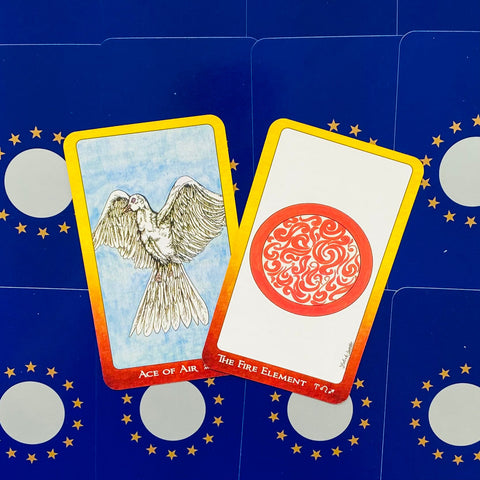 Tarot kortos, dvi fronte atidengtos: Ace of Air su balandžiu ir The Fire Element su raudonu ornamentu, geltoni rėmai ant mėlyno fono
