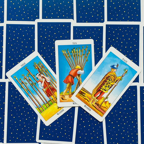 Tarot kortos Rider–Waite stiliaus, trys lazdų kortos centre (Nine, Ten, Page), išdėstytos ant mėlyno žvaigždėto fono