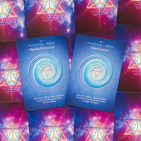 Kortos oracle: dvi atviros mėlynos priekinės kortos (Heart Centre, Reasses/Conscious) ant rožinės–violetinės kosminės nugarėlės