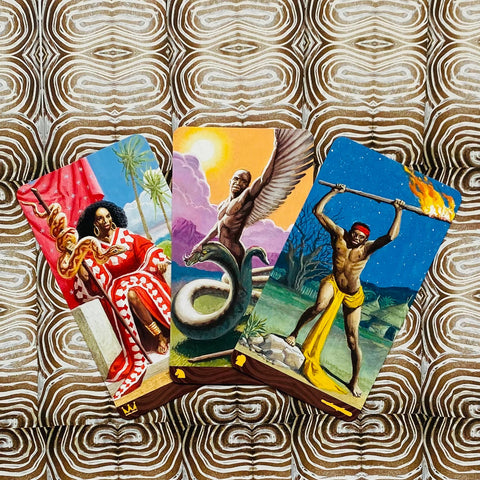 Tarot kortos trijų kortų išdėstymas su juodaodžių personažais: sėdinčia karaliene, sparnuotu angelu ir ugnimi besišaudančiu kariais