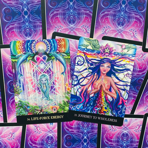 orakulo kortos, dvi atverstos spalvingos kortos (34 Life‑Force Energy ir 33 Journey to Wholeness) ant violetinio rašto fono, arti iš viršaus