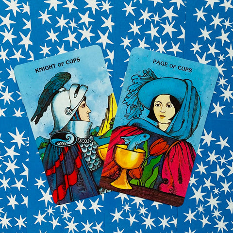 Tarot kortos dviejų kortų komplektas, ryškūs mėlyni Knight of Cups ir Page of Cups dizainai ant žvaigždėto fono, priekinis kampas