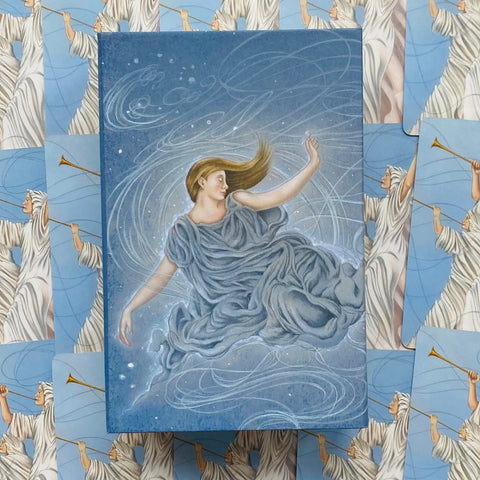 Tarot kortos su mėlyna dėžute, ant kurios svajinga moteris, pateiktos ant kortų nugarėlių su trimitininkais
