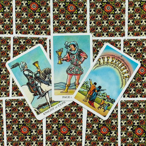 Tarot kortos Rider–Waite stiliaus: trys atverstos taurės kortos išdėstytos ant ornamentuoto juodo ir raudono fono, matomas kortų priekis