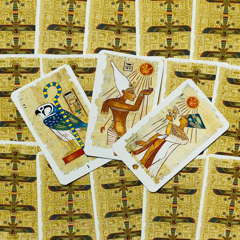 Tarot kortos Egipto motyvais, aukso ir smėlio atspalvių papiruso nugarėlės, trys kortos atvertos ir išdėstytos virš užverstų kortų