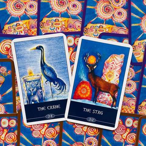 Tarot kortos dviejų kortų išklotinė su „The Crane“ ir „The Stag“ mėlynomis iliustracijomis ir spalvingu kortų fonu