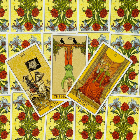 Tarot kortos su geltona rožių nugarėle, fanuotos ant stalo; matomos Major Arcana: Mirtis, Pakabintas žmogus ir Teisingumas