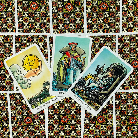 Tarot kortos Rider–Waite stiliaus trys atverstos kortos (Pentaklių tūzas, Karalius taurėse, Karalienė taurėse) ant raštuotos galinės pusės, matomas artimas kampinis išdėstymas