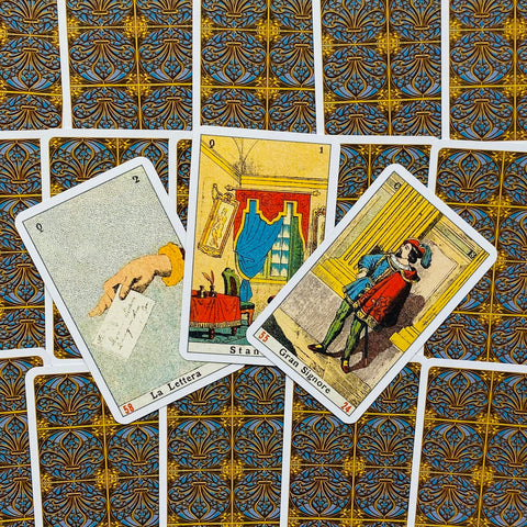 Tarot kortos komplektas su ornamentuotomis auksinėmis ir mėlynomis nugarėlėmis, kompozicija trijų atverstų kortų rodoma iš viršaus