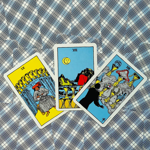 tarot kortos Rider–Waite, trys atvertos taurės kortos išdėstytos iš viršaus ant mėlyno raštuoto fono, pabrėžiant priekinį iliustracinį dizainą ir ryškias spalvas