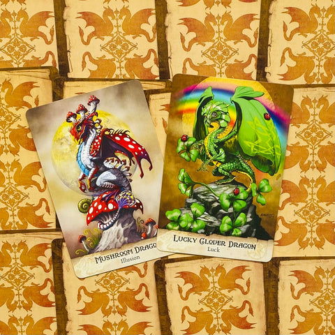 Orakulo kortos: raudonai dėmėta Mushroom Dragon ir žalia Lucky Clover Dragon kortos iš viršaus, pabrėžia skirtingus dizainus