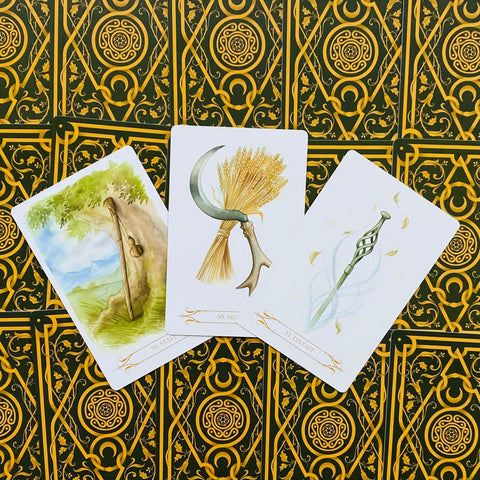tarot kortos — trys frontinės kortos su žaliu ir auksiniu raštuotu fonu, skirtingų lazdų ir javų iliustracijos, artimas kampas