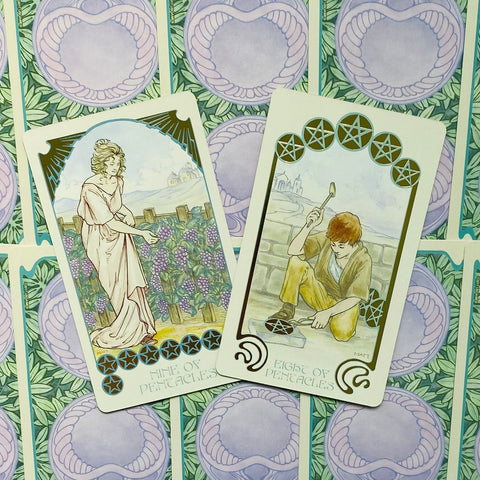 Tarot kortos, atverstos 8 ir 9 pentaklių versijos su akvarelinėmis pastelinėmis iliustracijomis ant žalio‑mėlyno fono