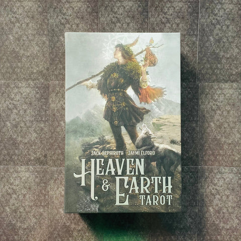 Heaven & Earth Tarot kortų dėžutės priekinis vaizdas su keliautojo figūra ir vilku, vertikalus planas ant raštuoto fono