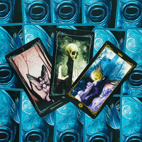 tarot kortos – tamsiai mėlyno nugarėlių dizaino komplektas, trys atvertos kortos parodytos kampu: kaukolė, fėja ir pentaklis