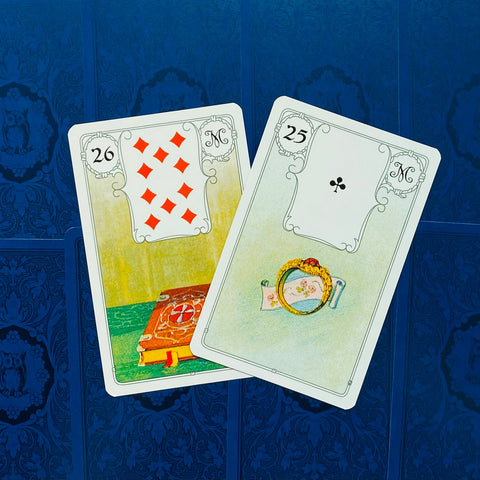 Kortos Lenormand, dvi atverstos kortos (25 Žiedas, 26 Knyga) ant mėlyno ornamentuoto fono, kampu išdėstytos