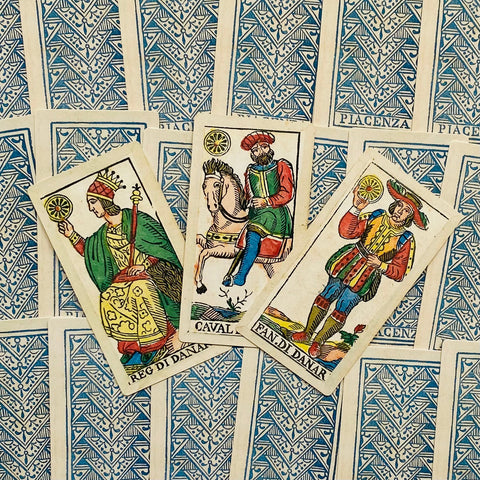 Kortų rinkinys Piacenza su mėlynomis nugarėlėmis, trys monetų figūrinės kortos (karalius, riteris, bernelis) išdėstytos ant atverstų kortų