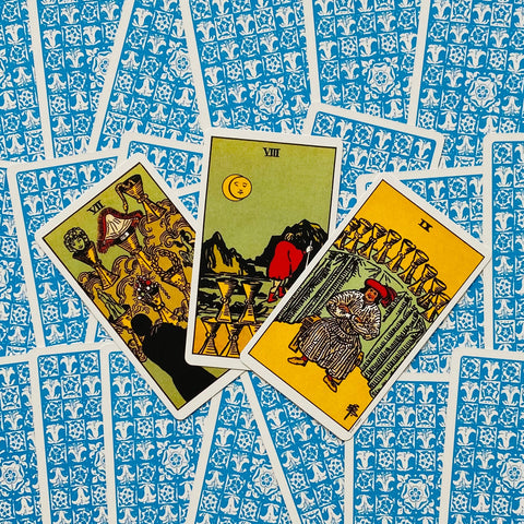 Tarot kortos rinkinys su ryškiomis taurų kortomis ir mėlynomis nugarėlėmis, trijų kortų išklotinė rodoma
