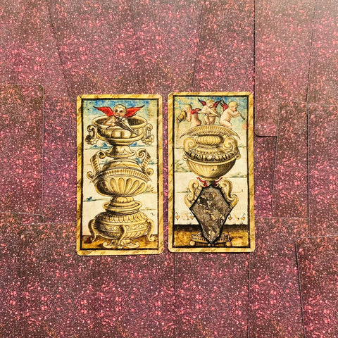 Kortos vintažinės tarot, dvi atverstos taurės kortos su ornamentuotu auksiniu‑kreminiu dizainu, centrinis išdėstymas