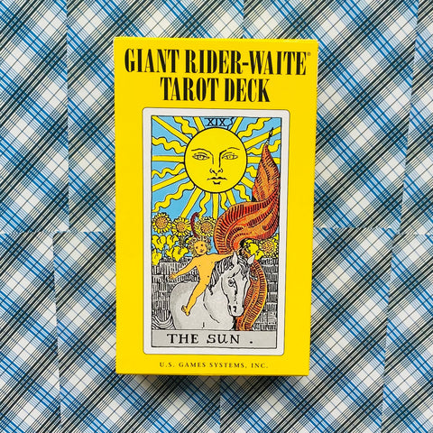 Giant Rider–Waite tarot kortų rinkinys geltoname dėkle su „The Sun“ kortos viršeliu, frontinis vaizdas ant mėlyno languoto fono